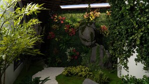 Um jardim com caminho de cascalho, diversas plantas e um elemento decorativo em pedra.