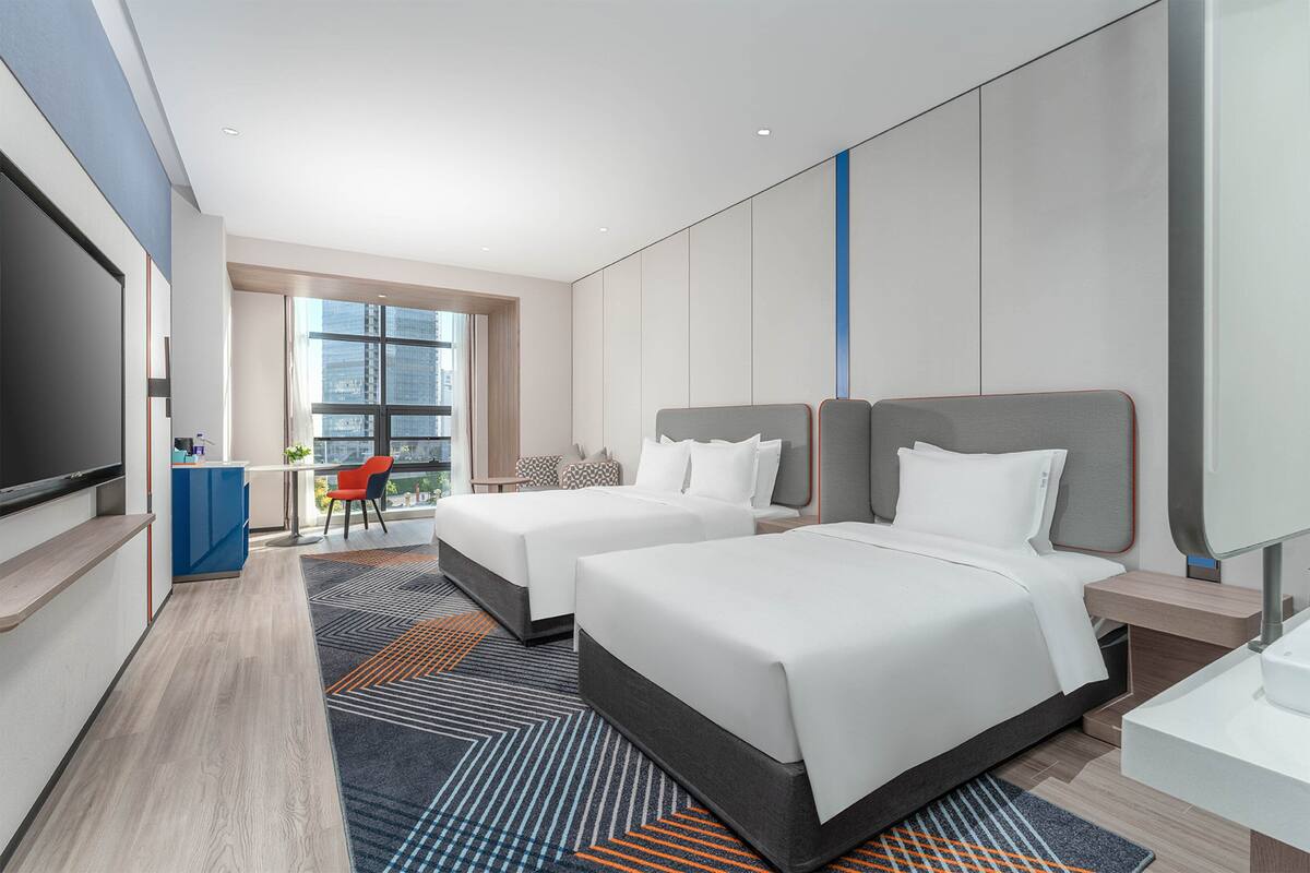 Une chambre d’hôtel avec deux lits, une télévision, un bureau et une vue sur la ville.