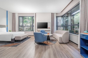 A modern hotel room with a bed, two armchairs, a sofa, a TV, and large windows with a view of greenery. - Holiday Inn Express Yinchuan Yuehai by IHG (Yinchuan)