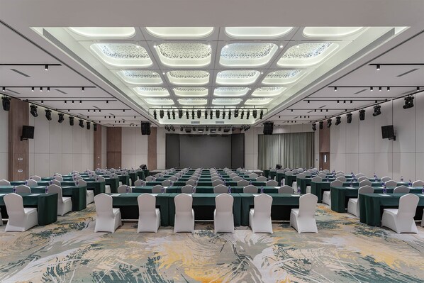 Un salón de conferencias con varias mesas, sillas blancas y una alfombra estampada.