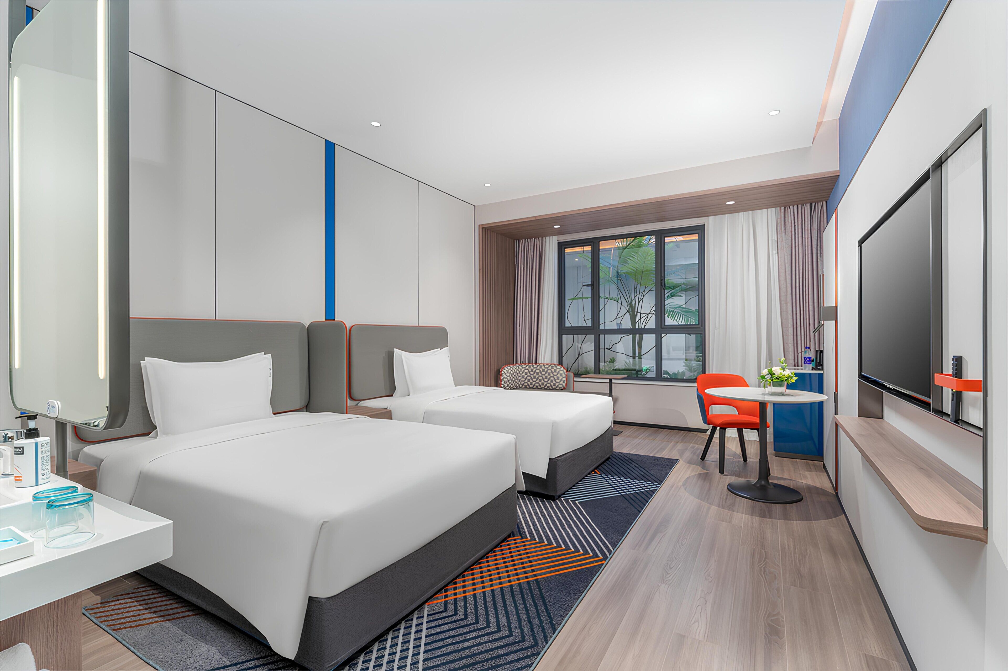 Habitación de hotel con dos camas, un escritorio, un televisor y una ventana con cortinas.