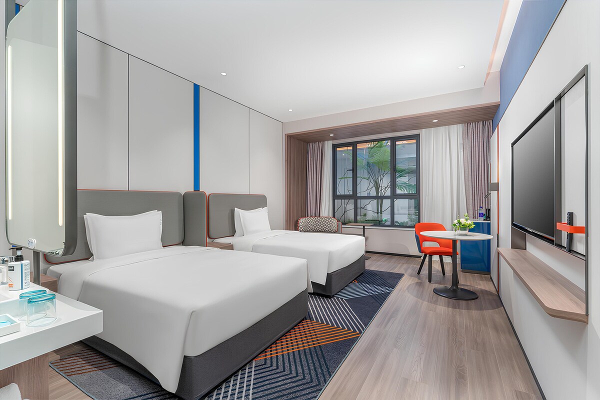 Een hotelkamer met twee bedden, een bureau, een televisie en een raam met gordijnen.