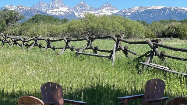 A rustic outdoor seating area with wooden chairs and tables, a fire pit, and a view of snow-capped mountains. - Teton View Tent (Tetonia)