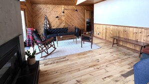 Een gezellige kamer met een houten plafond, een bank, een schommelstoel en een lange bank.