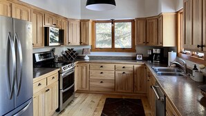 Een moderne keuken met houten kastjes, roestvrijstalen apparatuur en een groot raam.