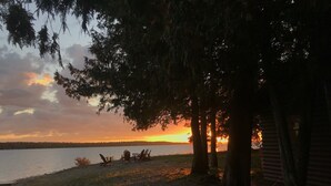 Uitzicht op een meer met een zonsondergang, bomen en een gebouw op de achtergrond.