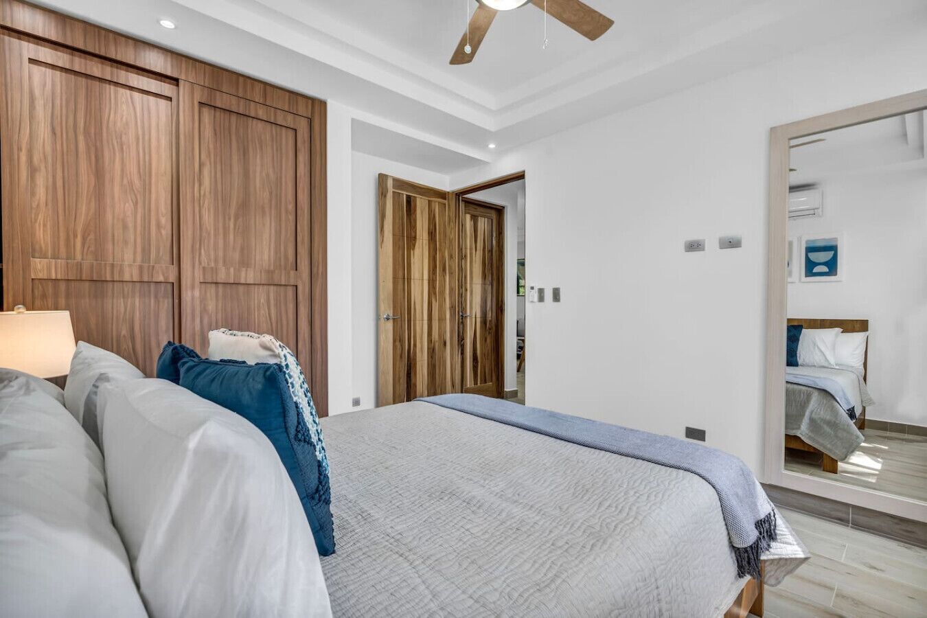 Une chambre avec un grand lit, une armoire en bois et un ventilateur de plafond.