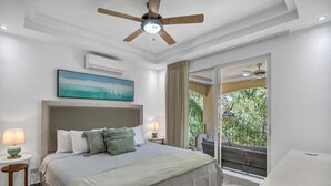 A modern bedroom with a large bed, a ceiling fan, a painting, and a balcony with a view of greenery. - Gav4: New Condo in Location Walkable to Beach (Tamarindo)