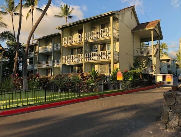 A multi-story hotel with balconies, surrounded by palm trees and a well-maintained lawn.