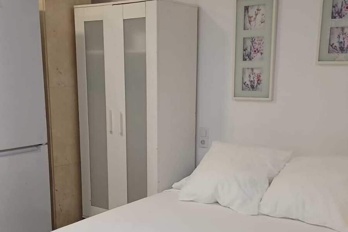 A bedroom with a bed, white curtains, and a wardrobe.