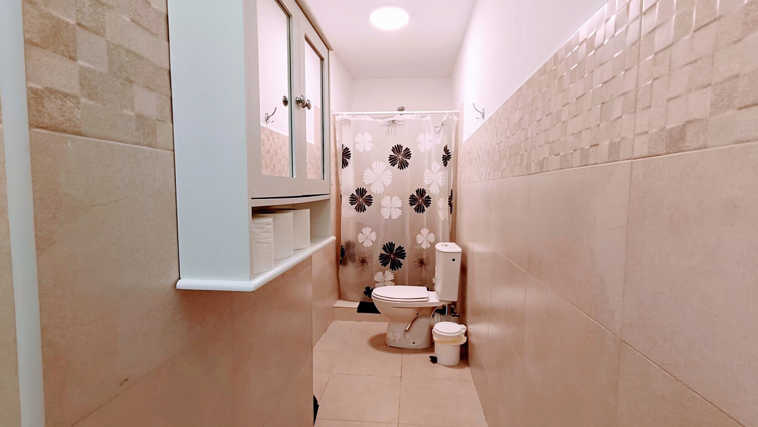 Um banheiro pequeno com vaso sanitário, cortina de chuveiro estampada com flores e prateleira com toalhas.