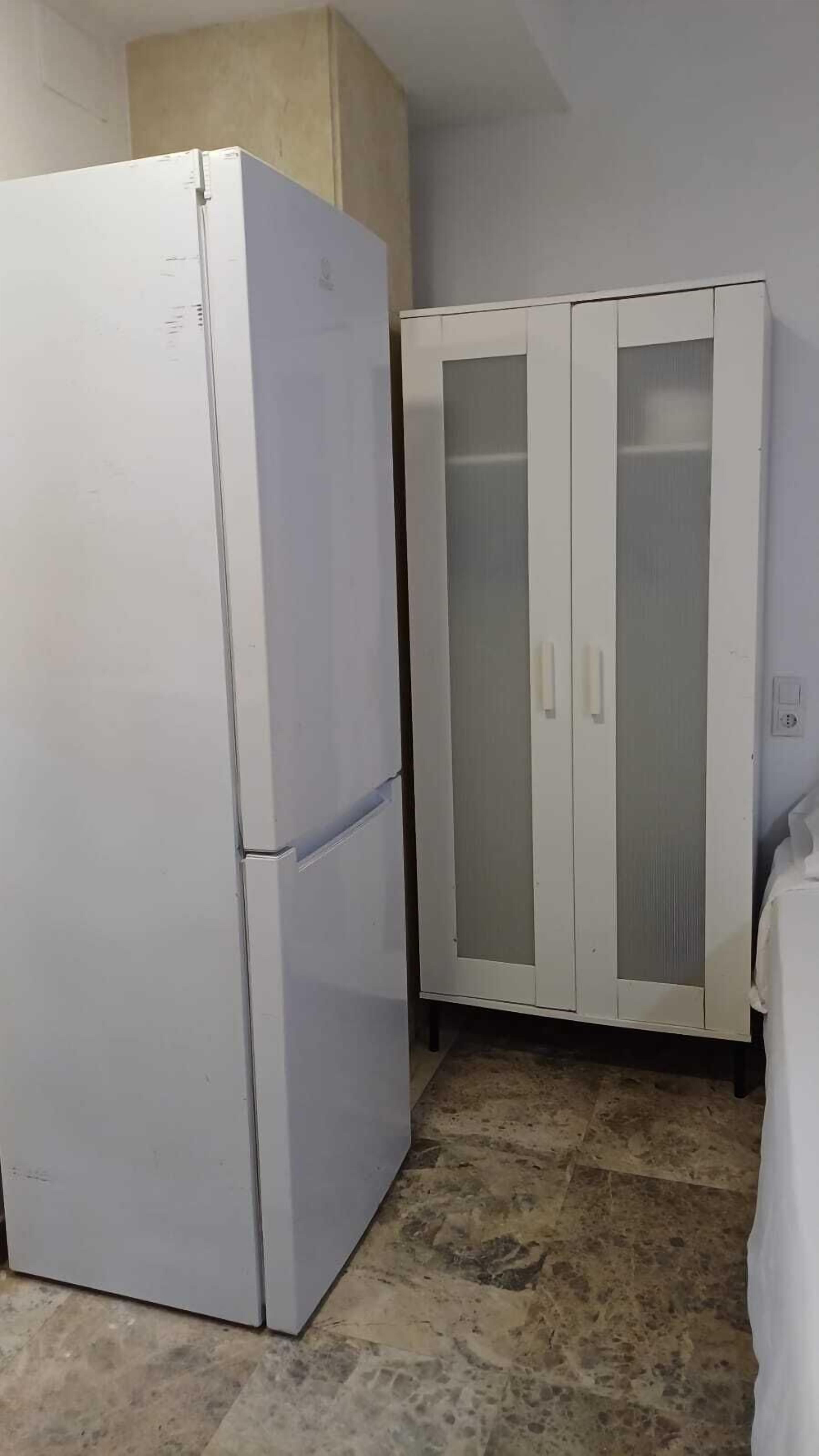 Una habitación compacta con un refrigerador blanco y un armario blanco con puertas de cristal.