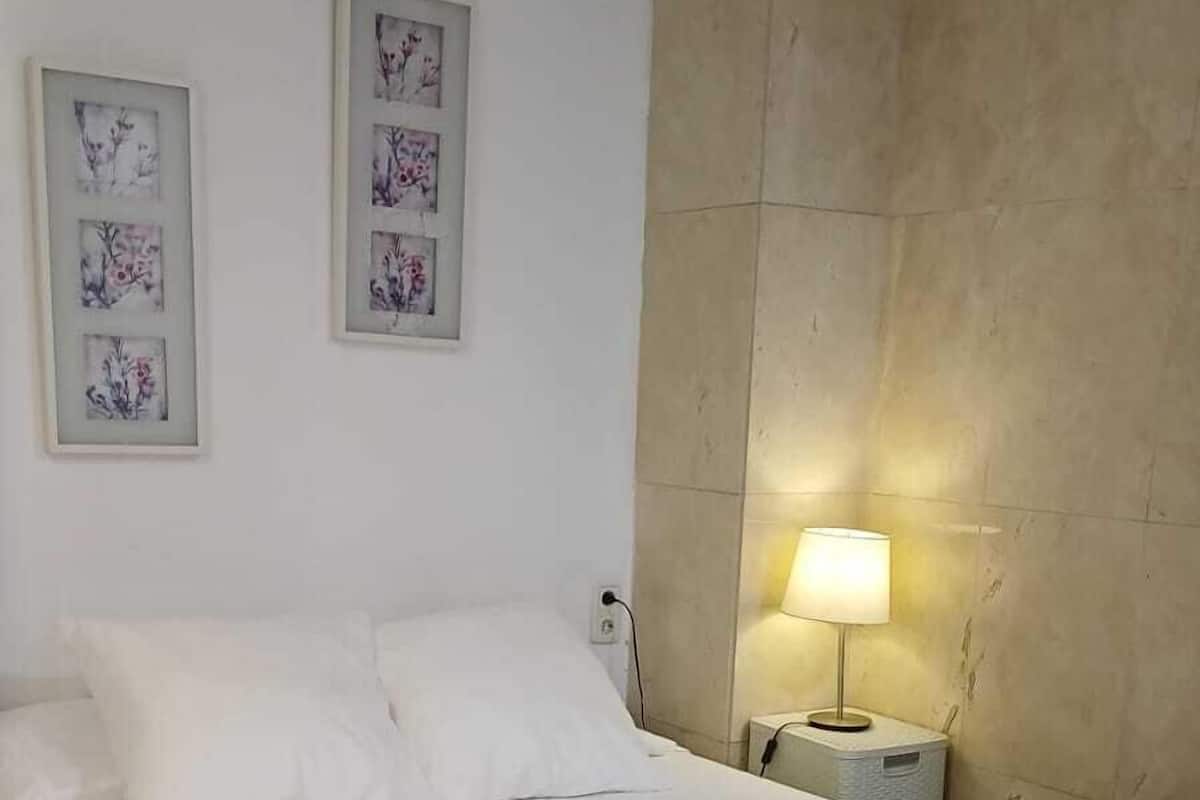 A neatly made bed with white linens in a room with a large beige headboard and two framed floral artworks on the wall.