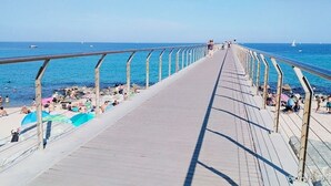 Una passera de fusta que condueix a una platja on la gent es relaxa i pren el sol.