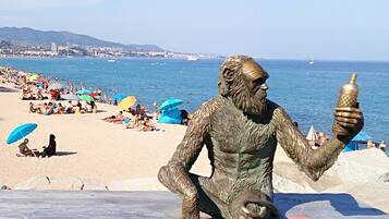 Una estatua de bronce de un hombre sosteniendo una botella sobre una pasarela de madera, con una playa y el océano al fondo.