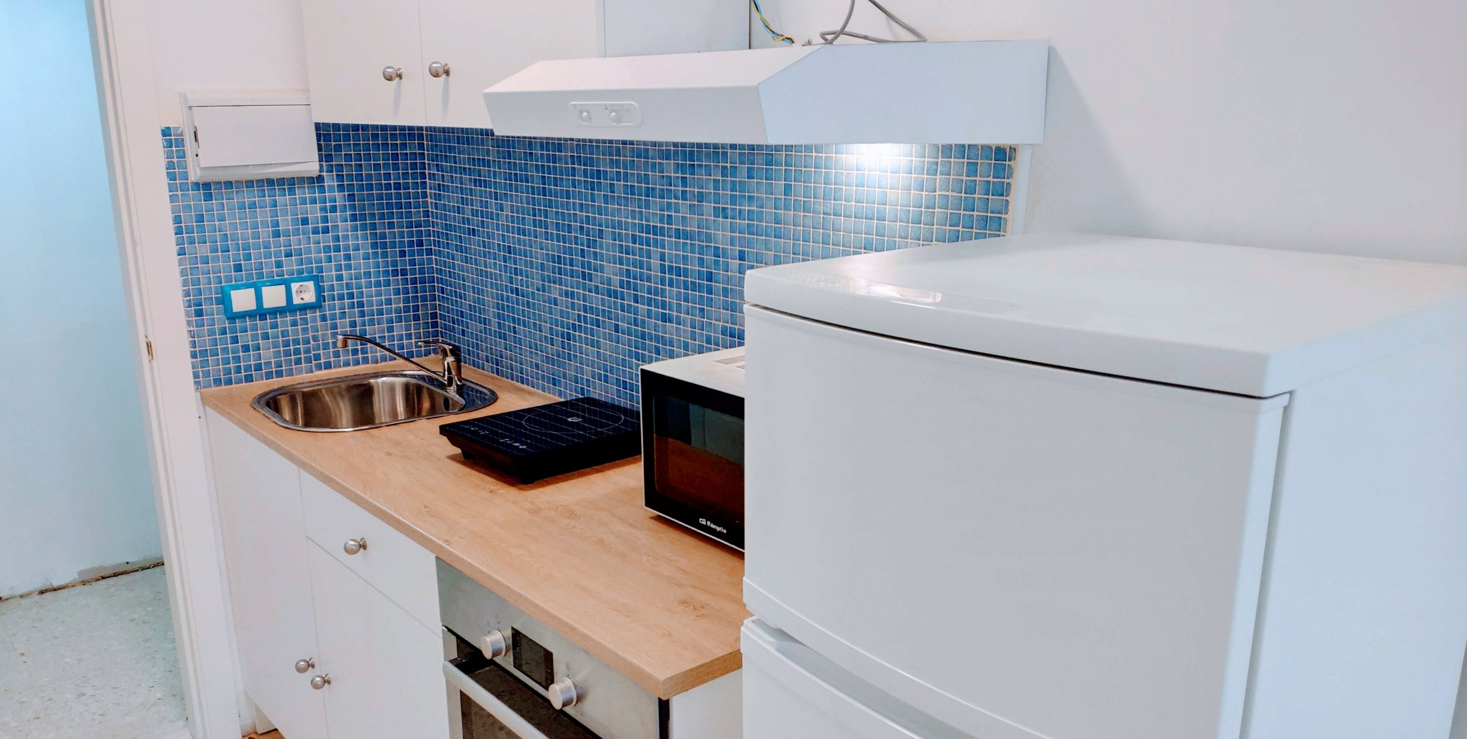 Eine kleine Küche mit Spüle, Mikrowelle und einem weißen Kühlschrank.