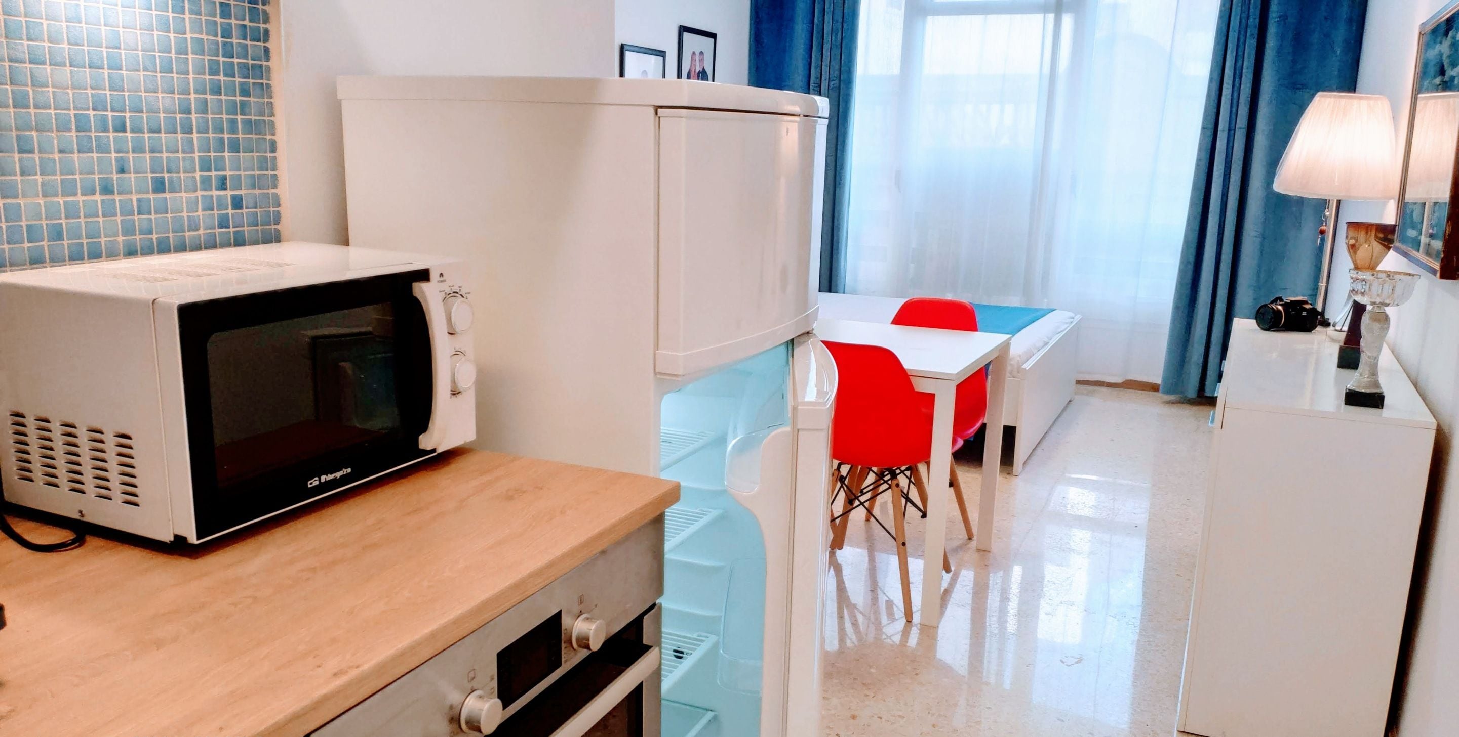 A compact kitchen with a microwave, refrigerator, and a dining area with red chairs.