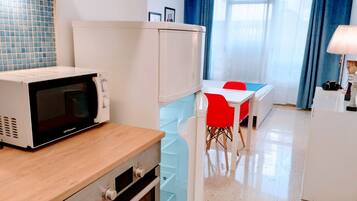 A compact kitchen with a microwave, refrigerator, and a dining area with red chairs.