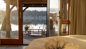 A bedroom with a large sliding glass door leading to a balcony with a view of a lake and trees. - Private beach luxury home sleeps 12, Shelton, WA (Shelton)