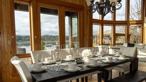 A dining area with a table set for six, large windows, and a view of a lake. - Private beach luxury home sleeps 12, Shelton, WA (Shelton)