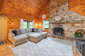 A cozy cabin interior with a stone fireplace, wooden walls, and a sectional sofa.