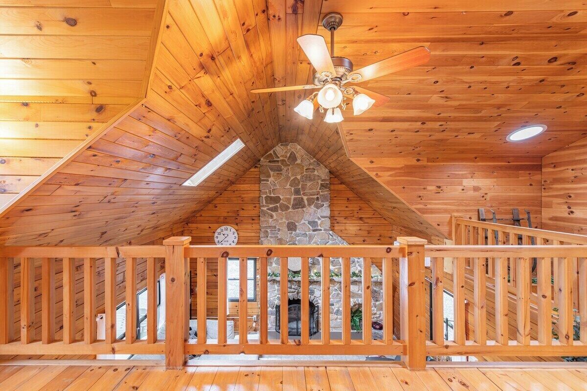 A wooden interior with a stone fireplace, wooden railing, and a ceiling fan.
