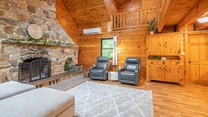 Interior d'una cabana de fusta amb una llar de pedra, seients de cuir i armaris de fusta.