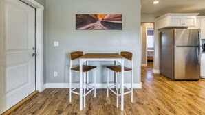 Une cuisine avec une table en bois et deux chaises, un réfrigérateur en acier inoxydable et un tableau accroché au mur.
