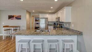 Une cuisine moderne dotée de plans de travail en granit, de meubles blancs et d’un îlot central avec des tabourets de bar.