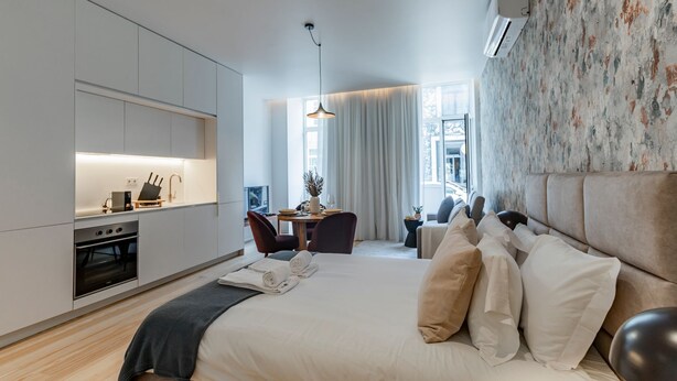 Ein modernes Hotelzimmer mit Küchenzeile, Essbereich und einem großen Bett mit vielen Kissen.
