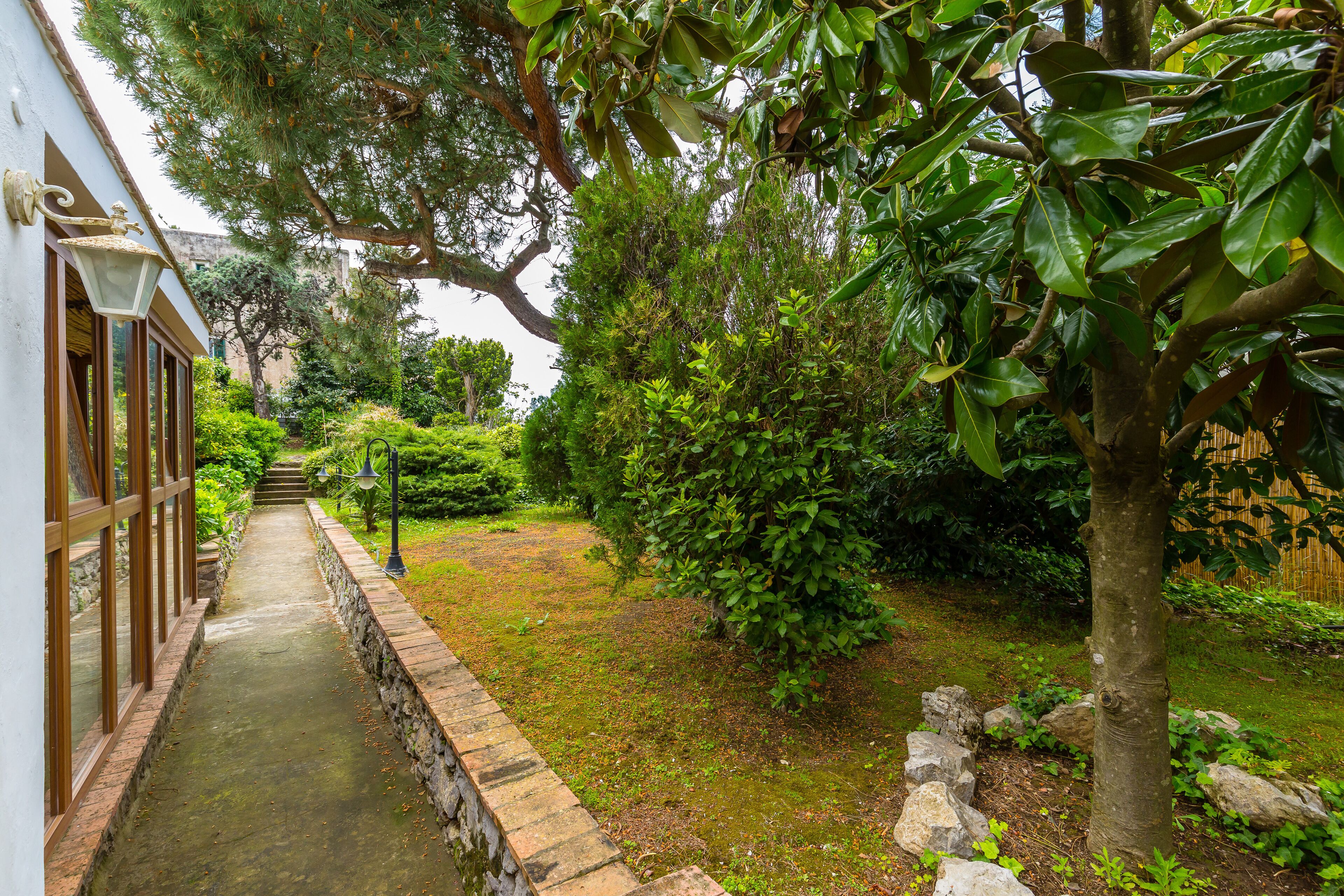 A pathway leading to a building with large windows and a stone wall.