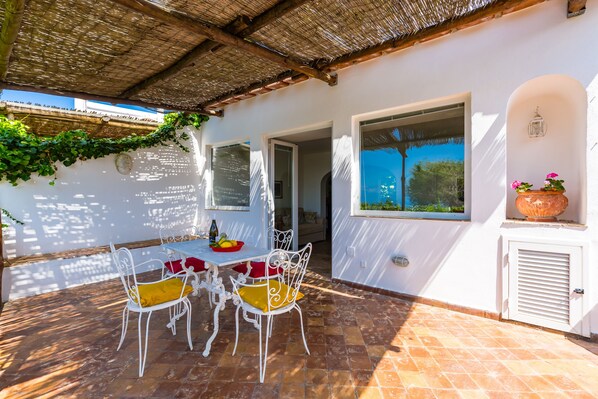 Une terrasse extérieure avec une table et des chaises, un toit de chaume et une vue sur la mer.