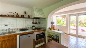 Een keuken met een betegelde spatwand, houten kastjes, een vaatwasser, een oven en een raam met uitzicht op een tuin.