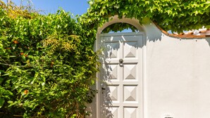 Een witte deur met een decoratieve handgreep, omringd door weelderige groene begroeiing.