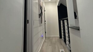 Un pasillo con paredes blancas, luces empotradas en el techo, una puerta a la izquierda y una escalera a la derecha.