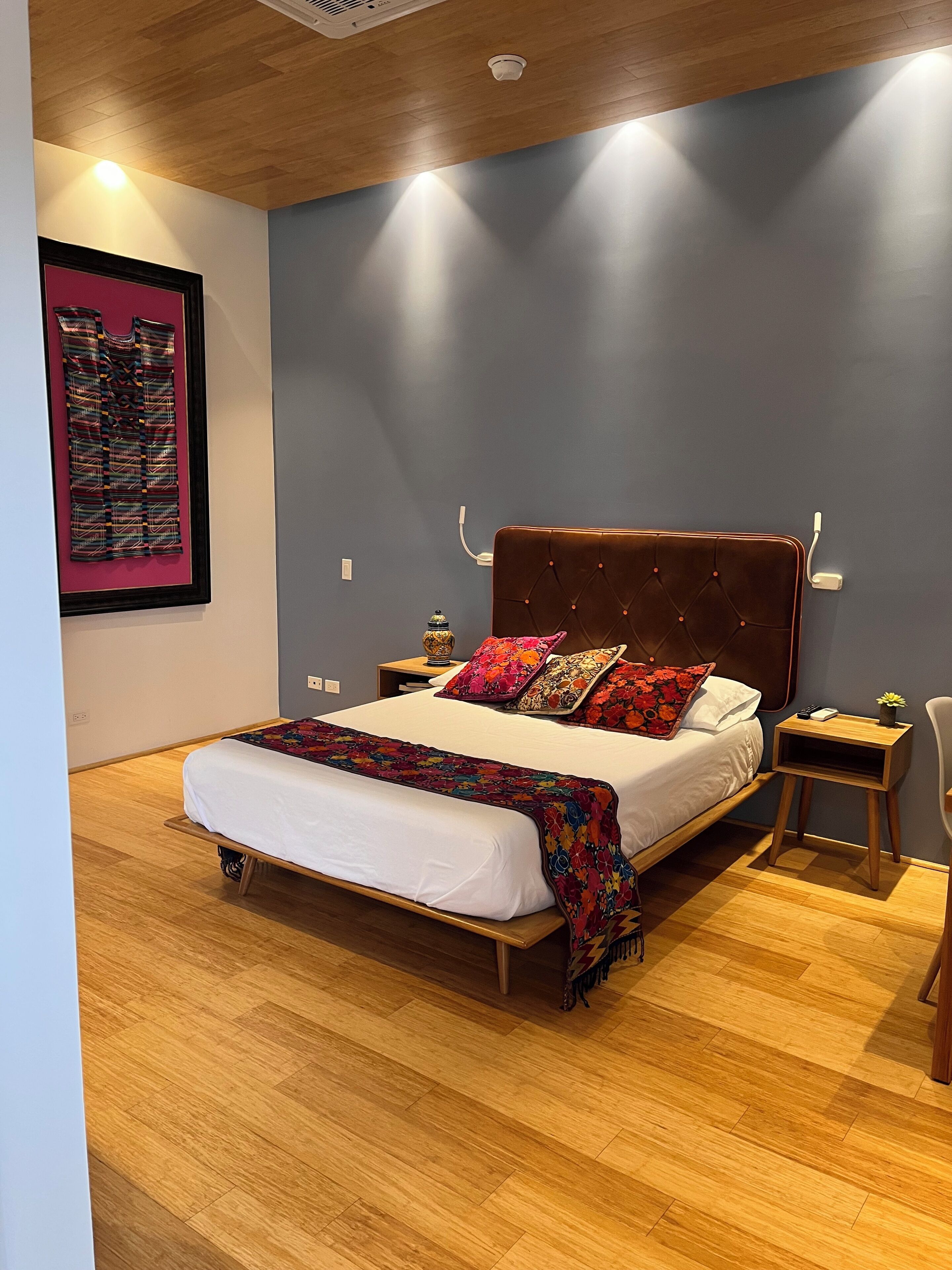 A modern bedroom with a wooden bed frame, a headboard with a tufted design, and a bedside table with a lamp and a vase of flowers.