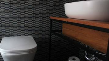 A bathroom with a toilet, a sink on a wooden shelf, and a patterned wall.