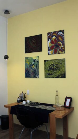 A room with a desk, four abstract paintings, a kettle, and a framed certificate.