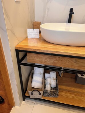 A bathroom with a white sink, wooden vanity, and storage shelves with towels and a basket. - Hotel Brecha (Tijuana)