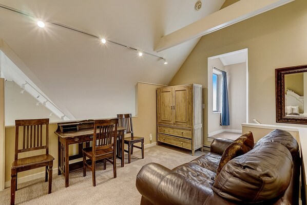 A loft bedroom with a sloped ceiling, a dining area with wooden furniture, a leather couch, and a large mirror. - Lodge at Mtn Village A204 | Ski-In/Out | Hot Tub | Valley View | Pool (Park City)