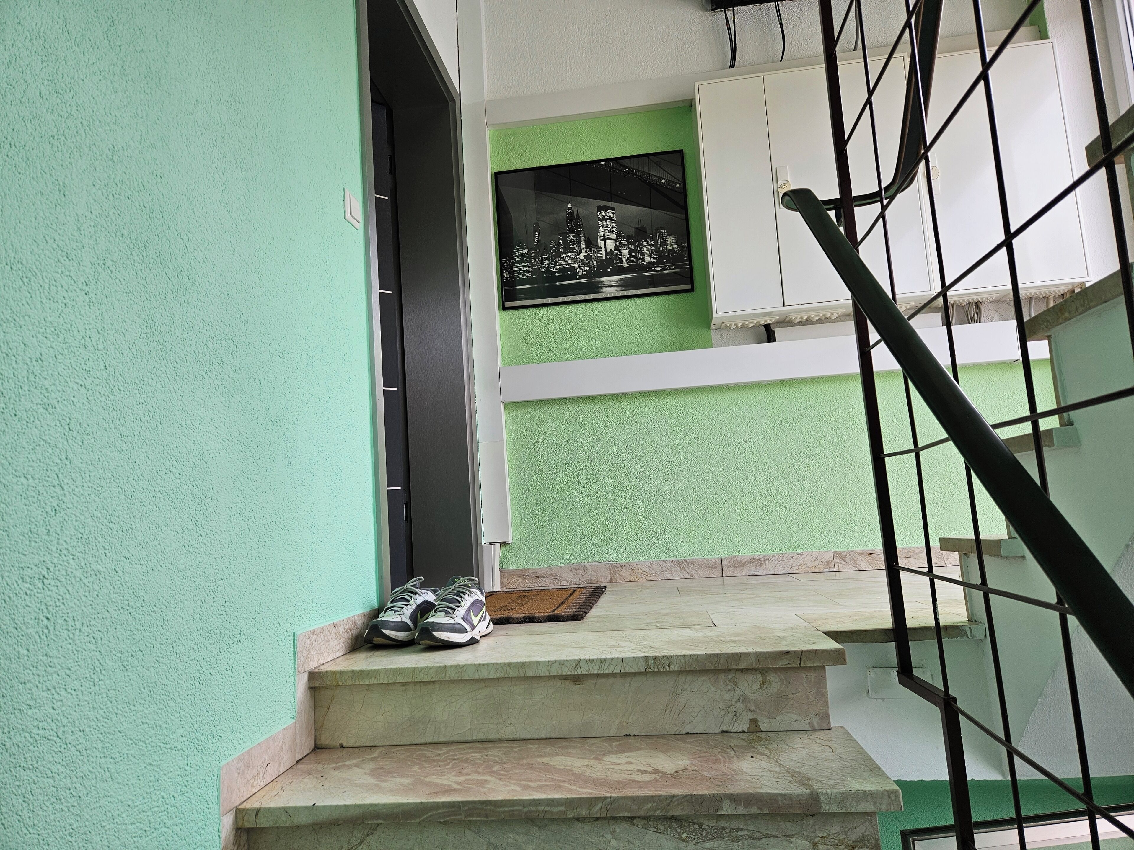 A staircase with a pair of shoes on the steps, a door, and a framed picture on the wall.