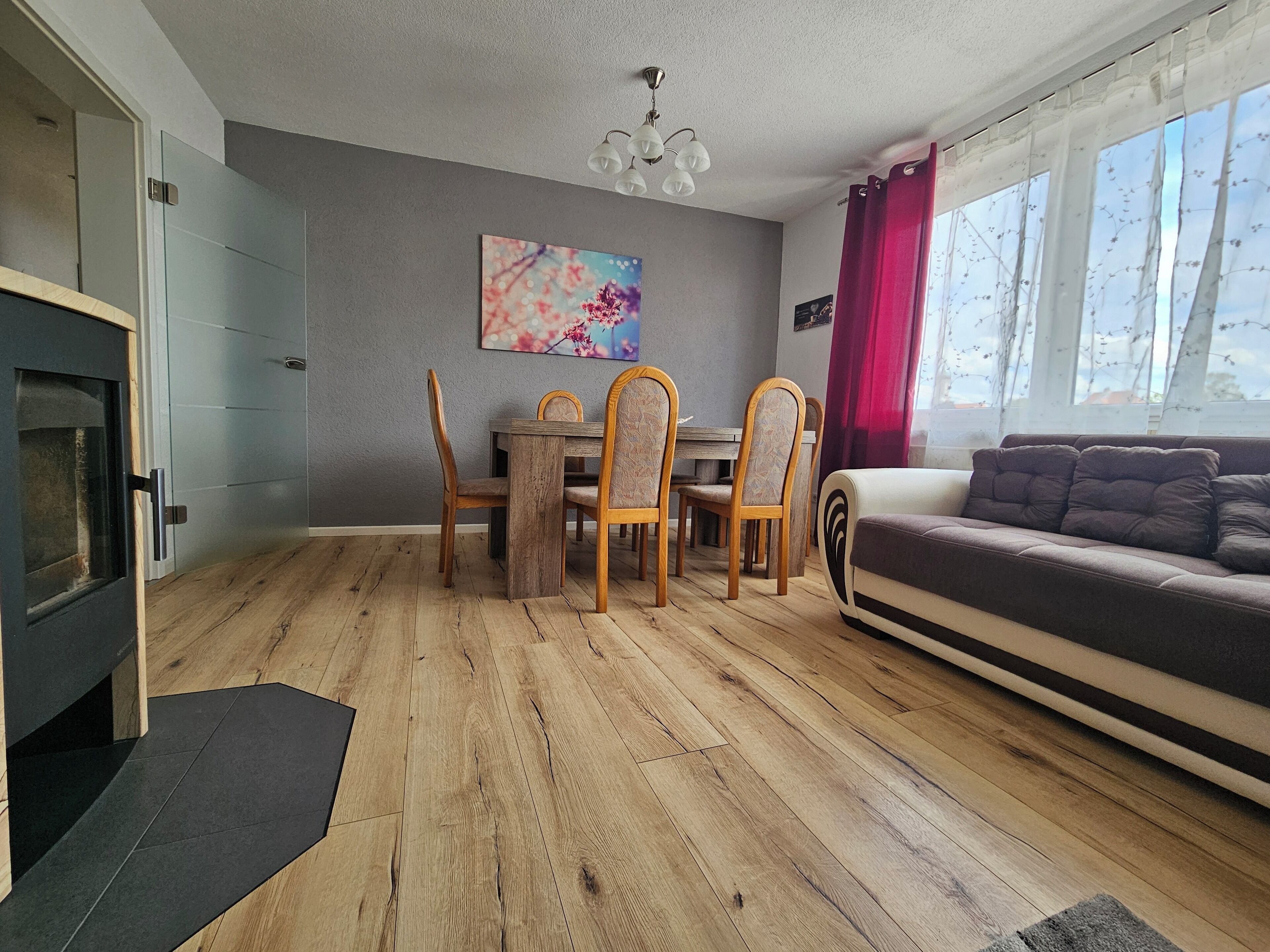 Ein modernes Wohnzimmer mit Holzboden, einem Essbereich mit Holzsesseln, einer Couch und einem Kamin.
