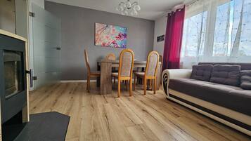 Ein modernes Wohnzimmer mit Holzboden, einem Essbereich mit Holzsesseln, einer Couch und einem Kamin.