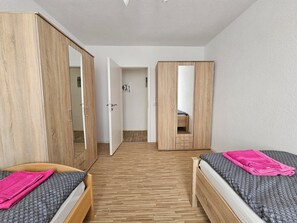 A bedroom with two beds, wooden wardrobes, and a mirror.