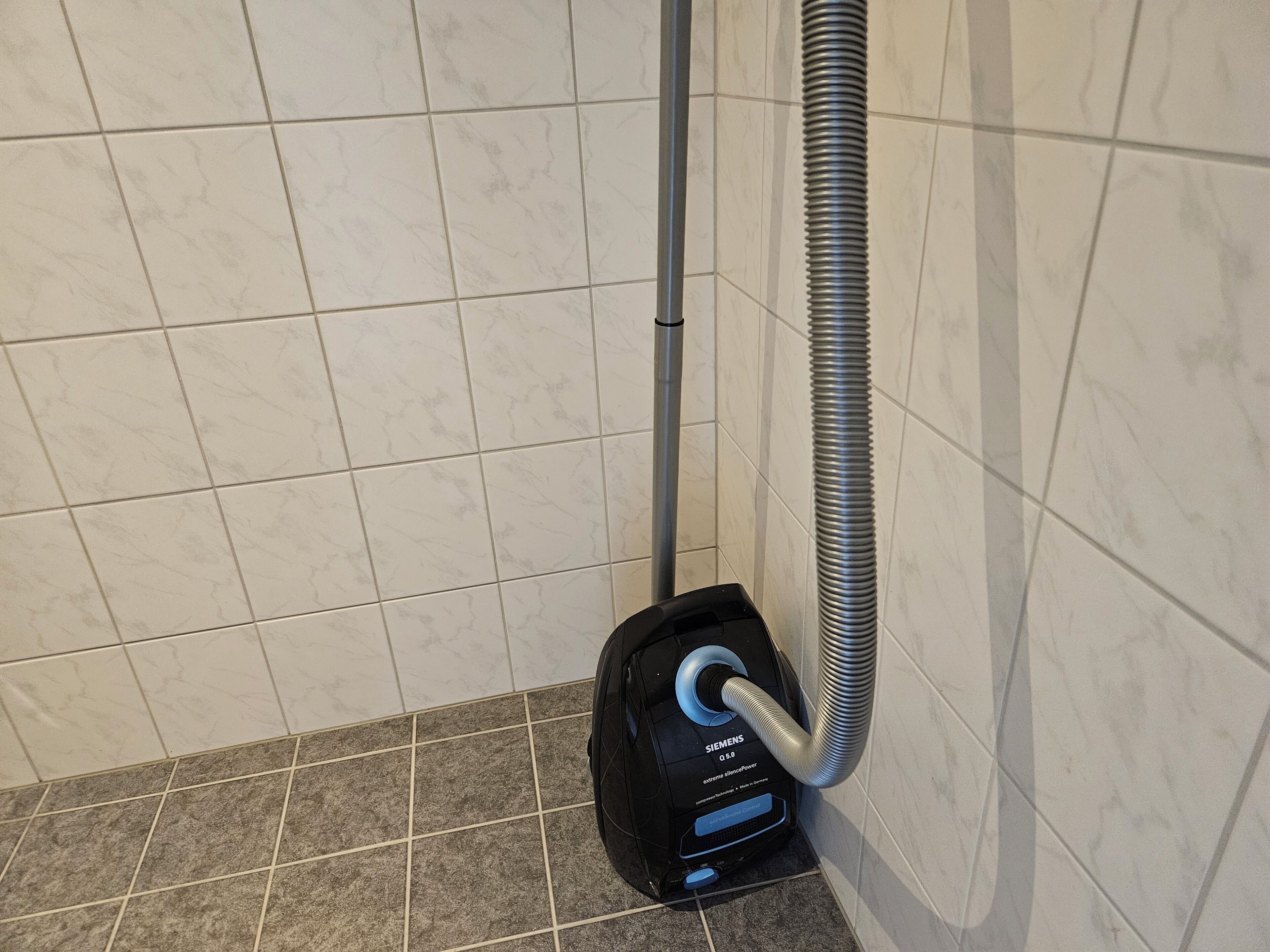 A vacuum cleaner in a bathroom with tiled walls and floor.