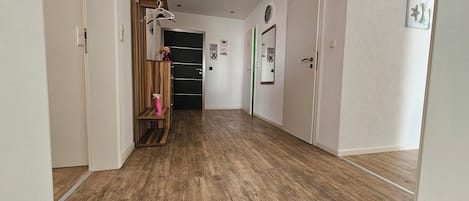 A hallway with wooden flooring, a coat rack, a door with a green handle, and a wall-mounted clock.