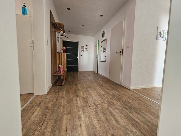 Un pasillo con piso de madera, un perchero, una puerta con picaporte verde y un reloj fijado a la pared.