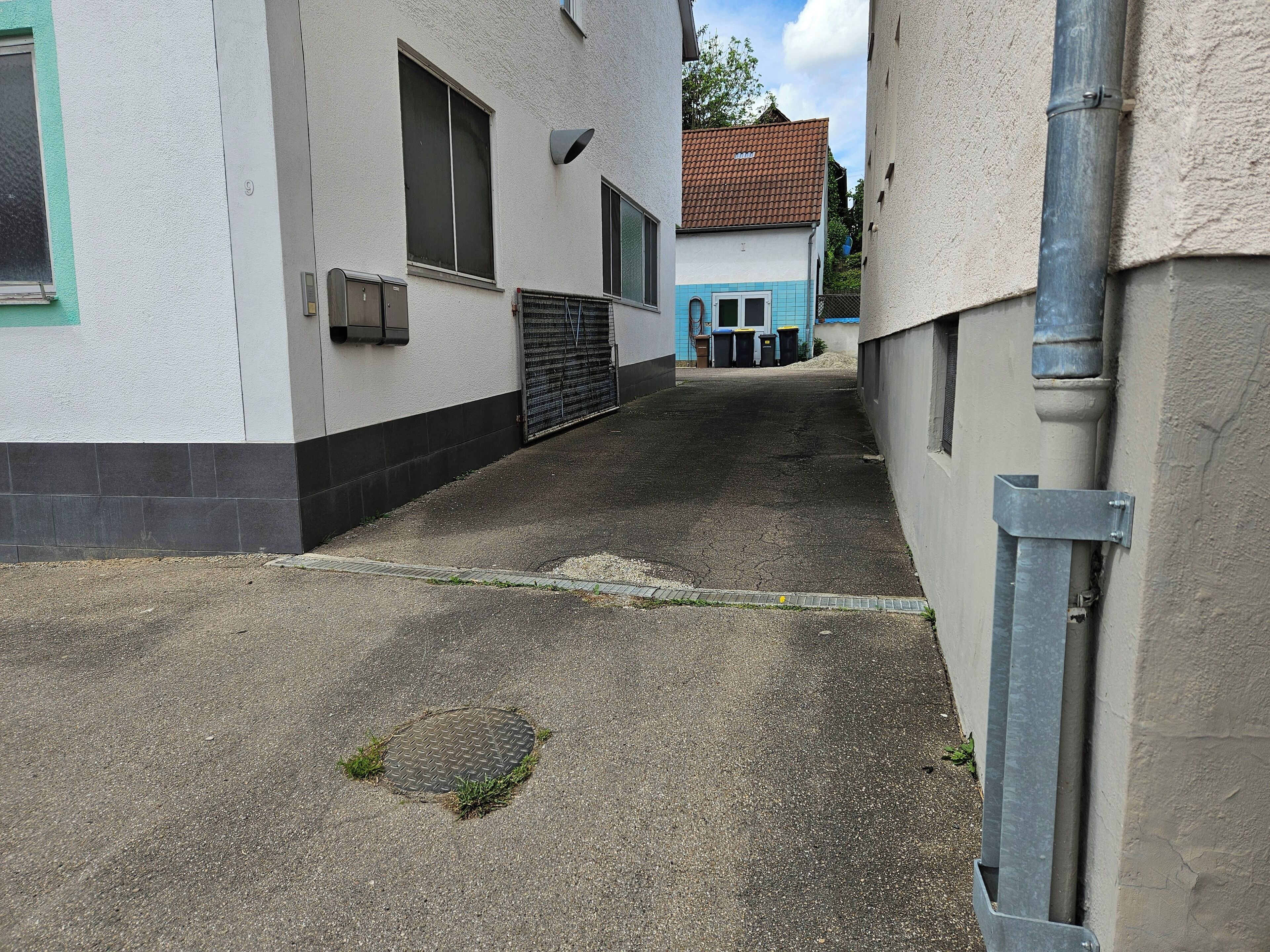A narrow alleyway between buildings with a metal grate and a manhole cover on the ground.