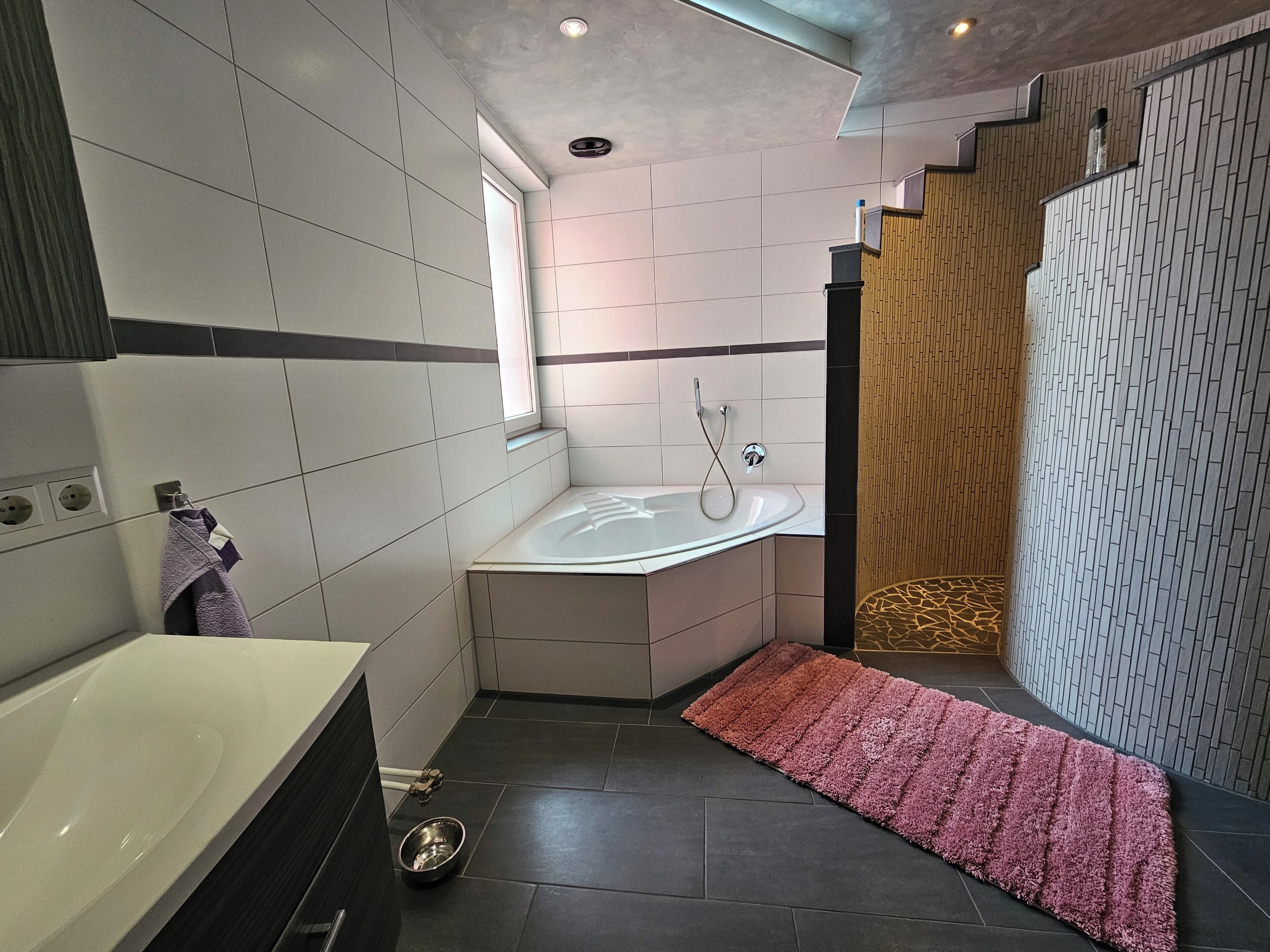 A modern bathroom with a bathtub, a large mirror, and a window.