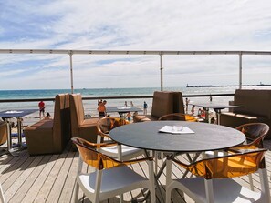 Un espacio de estar al aire libre con mesas y sillas, con vistas a la playa y el océano.